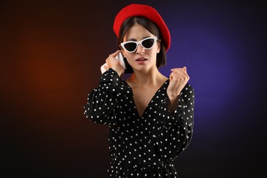 Stylish woman listening to voice message via smartphone on color background