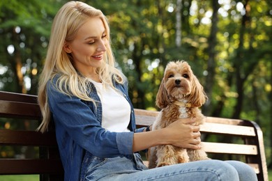 Beautiful young woman with cute dog on bench in park