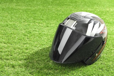 Photo of Modern motorcycle helmet with visor on green grass outdoors, space for text