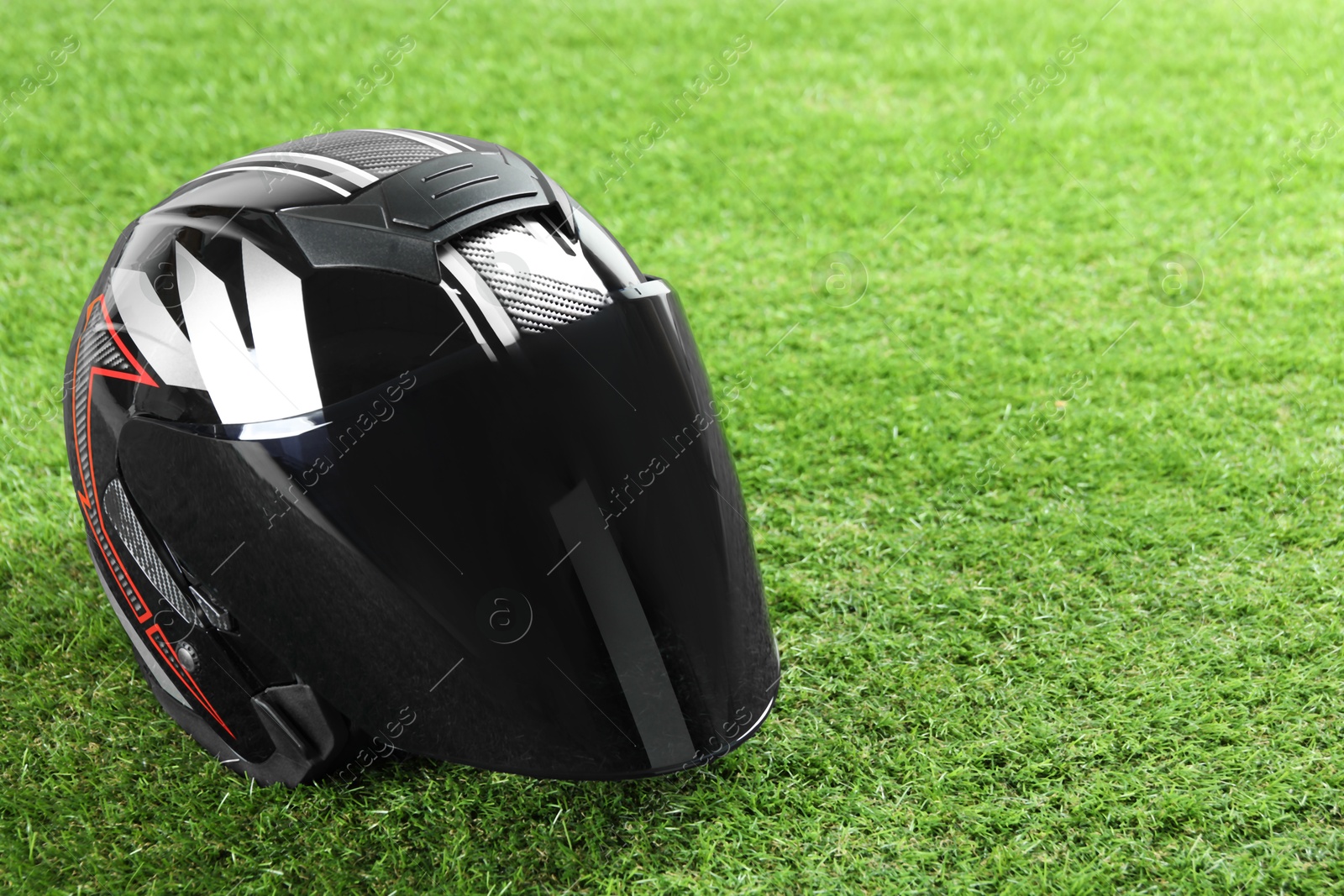 Photo of Modern motorcycle helmet with visor on green grass outdoors, space for text