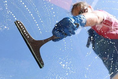 Photo of Woman washing window with squeegee tool against blue sky, closeup