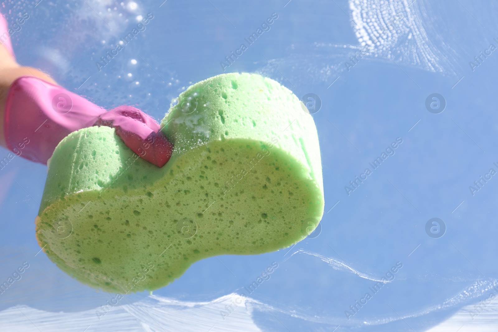 Photo of Woman washing window with sponge against blue sky, closeup