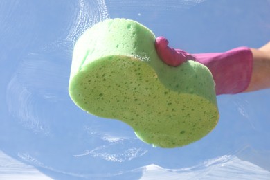 Photo of Woman washing window with sponge against blue sky, closeup