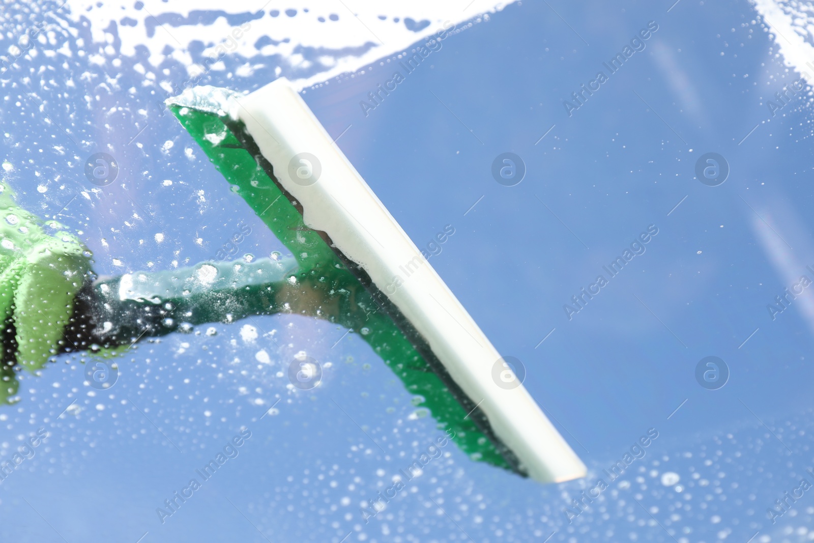 Photo of Woman washing window with squeegee tool against blue sky, closeup