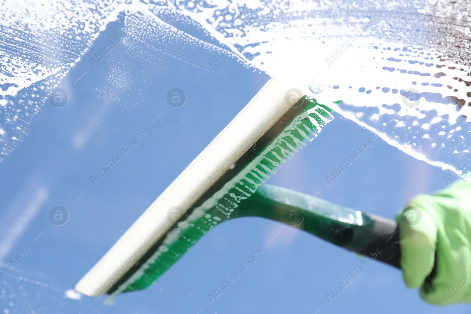 Photo of Woman washing window with squeegee tool against blue sky, closeup