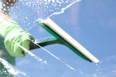 Photo of Woman washing window with squeegee tool against blue sky, closeup