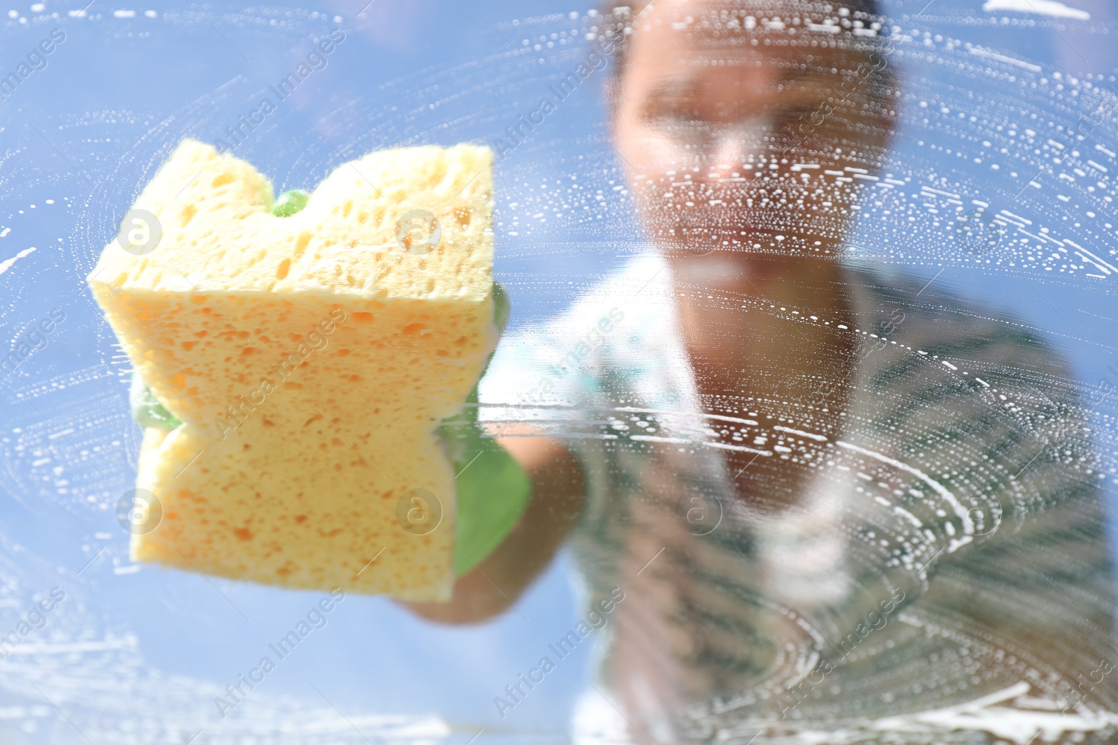 Photo of Woman washing window with sponge against blue sky, closeup