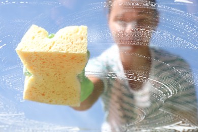 Woman washing window with sponge against blue sky, closeup