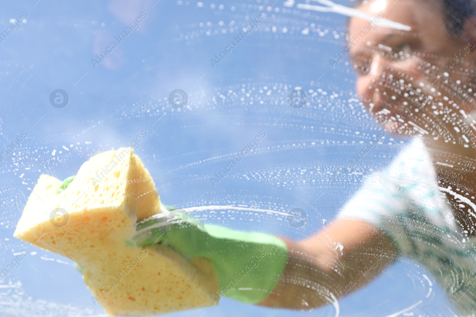 Photo of Woman washing window with sponge against blue sky, closeup