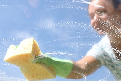 Woman washing window with sponge against blue sky, closeup