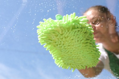 Woman washing window with microfiber mitt against blue sky, closeup