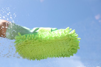 Woman washing window with microfiber mitt against blue sky, closeup