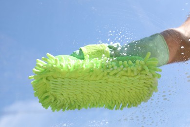 Photo of Woman washing window with microfiber mitt against blue sky, closeup