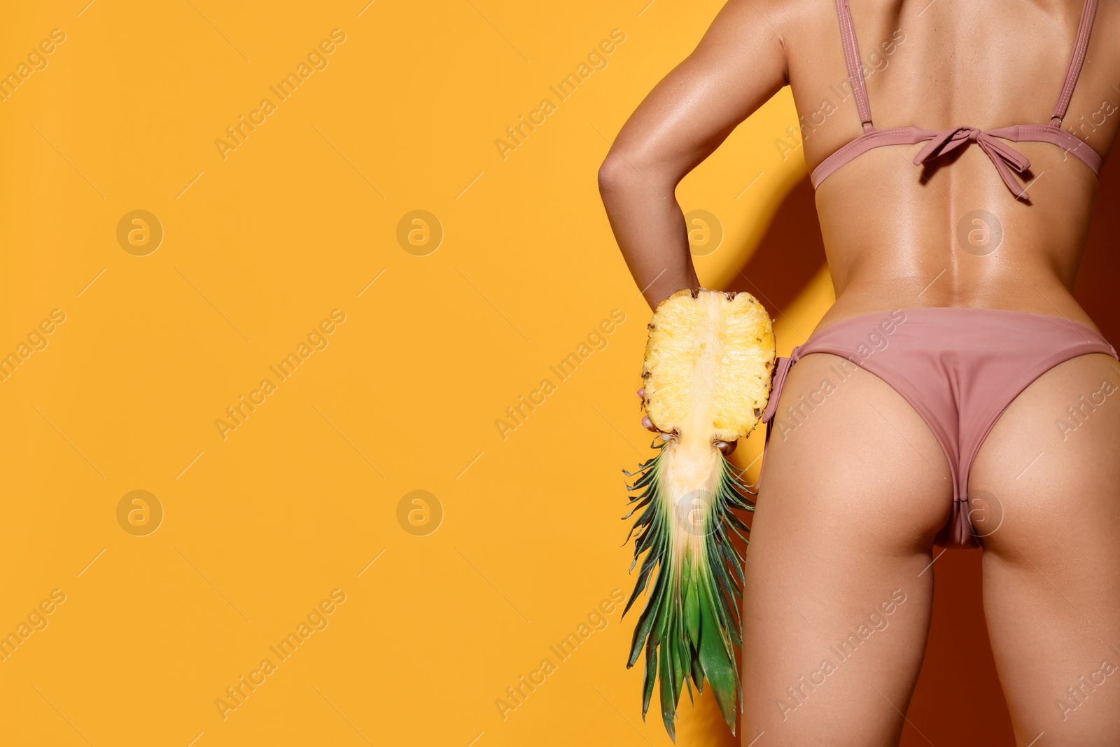 Photo of Woman in bikini with half of pineapple on orange background, closeup. Space for text