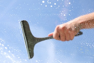 Woman washing window with squeegee tool against blue sky, closeup