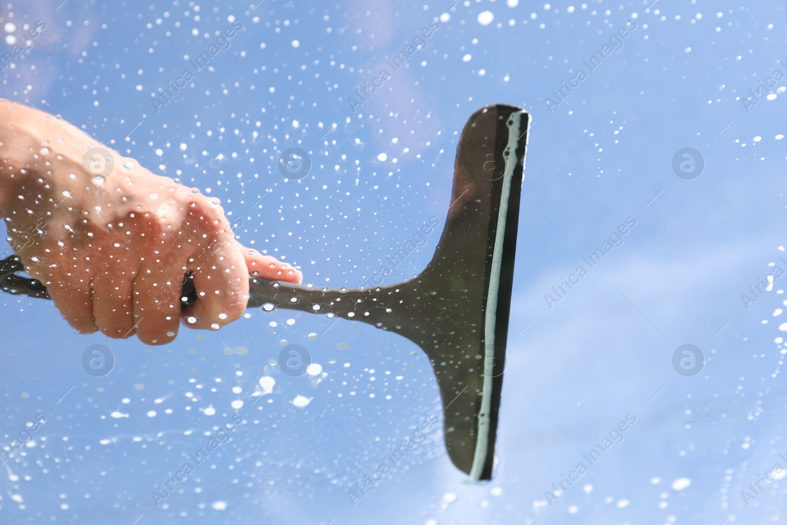 Photo of Woman washing window with squeegee tool against blue sky, closeup