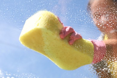 Woman washing window with sponge against blue sky, closeup