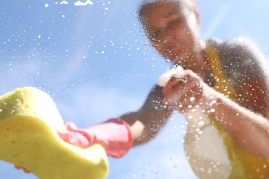 Woman washing window with sponge against blue sky, closeup