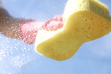 Woman washing window with sponge against blue sky, closeup