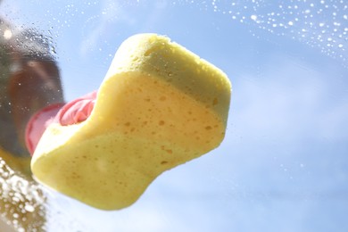 Woman washing window with sponge against blue sky, closeup