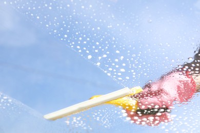 Photo of Woman washing window with squeegee tool against blue sky, closeup