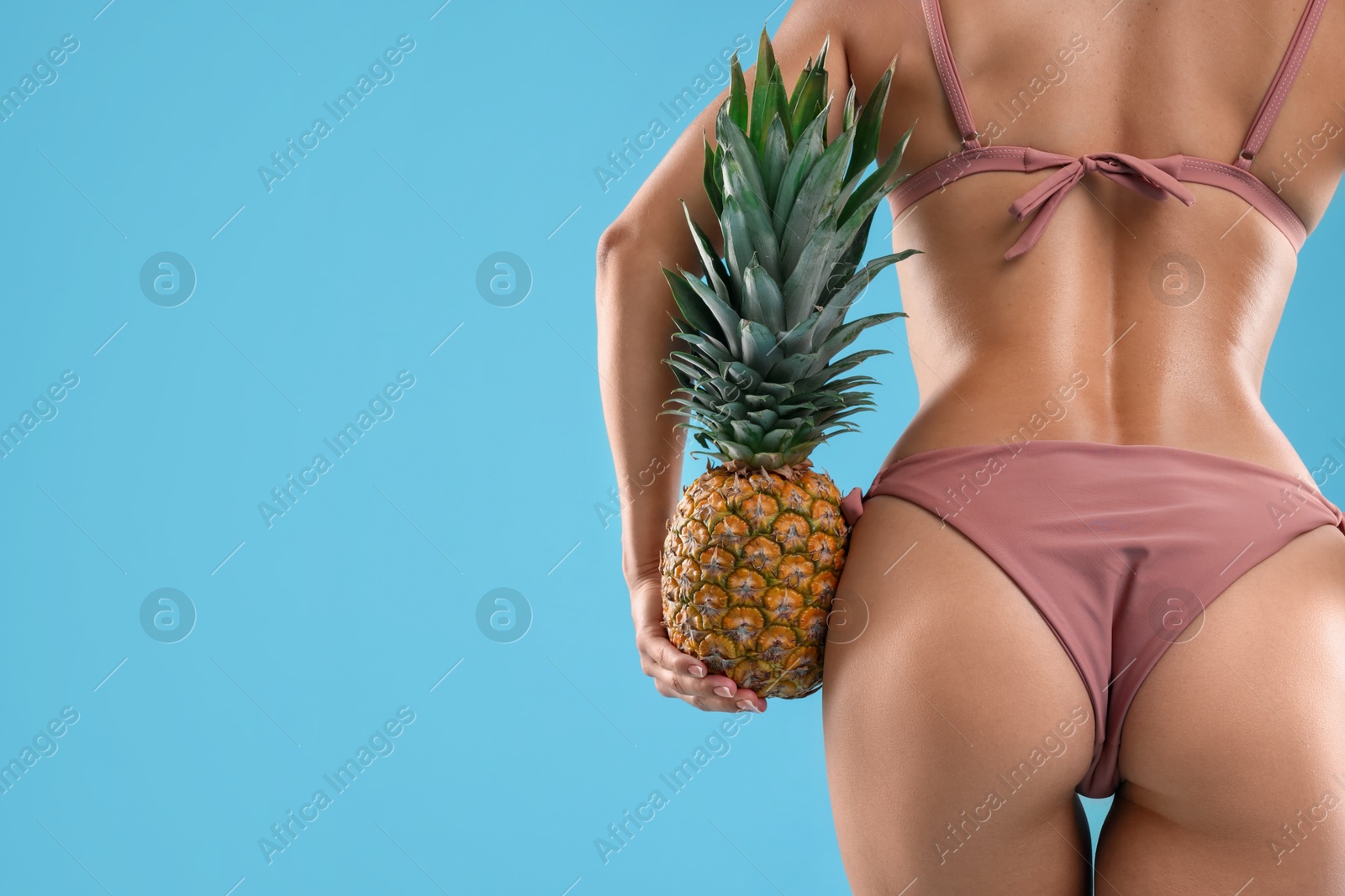 Photo of Woman in bikini with fresh pineapple on light blue background, closeup. Space for text