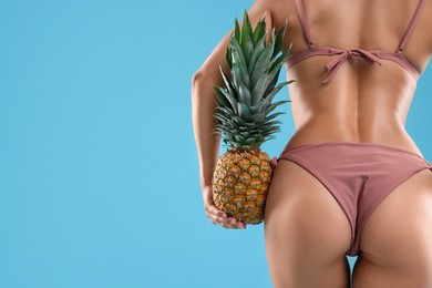 Woman in bikini with fresh pineapple on light blue background, closeup. Space for text