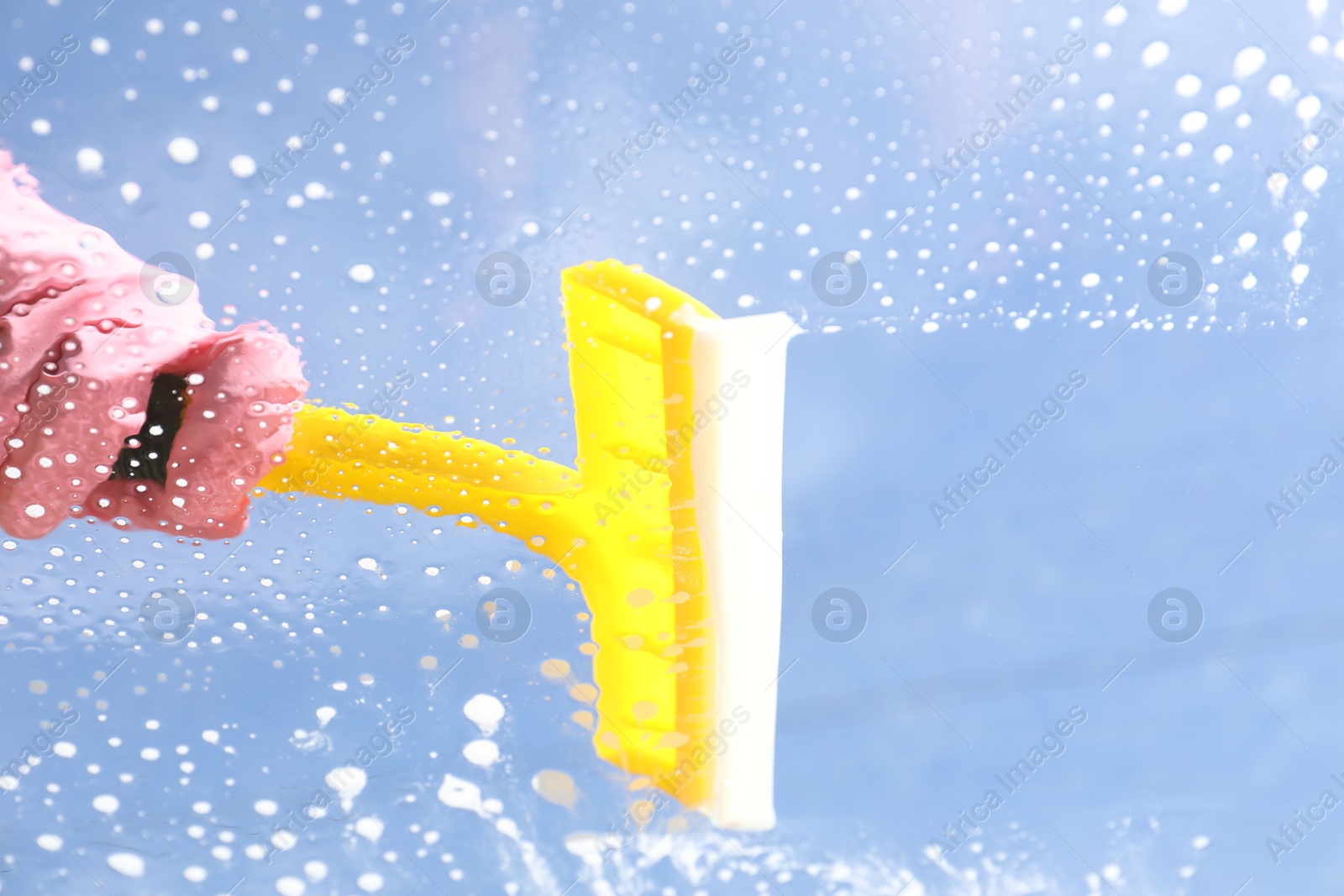 Photo of Woman washing window with squeegee tool against blue sky, closeup