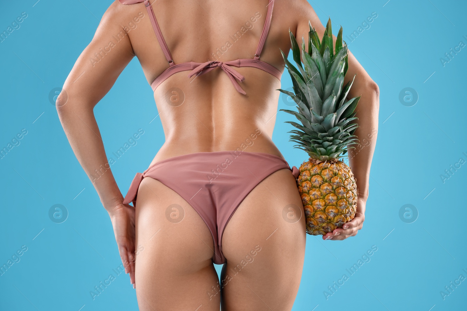 Photo of Woman in bikini with fresh pineapple on light blue background, closeup