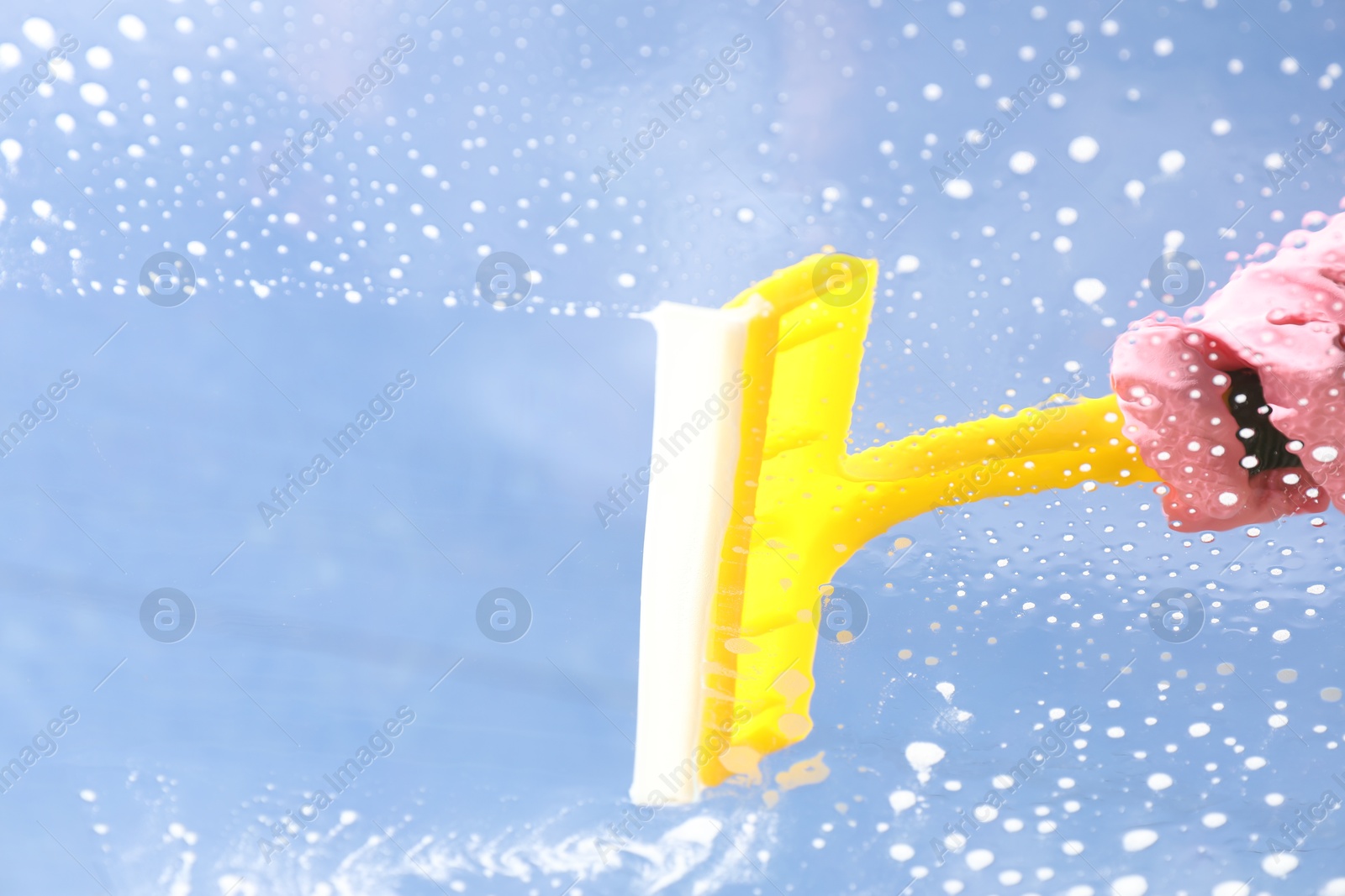 Photo of Woman washing window with squeegee tool against blue sky, closeup