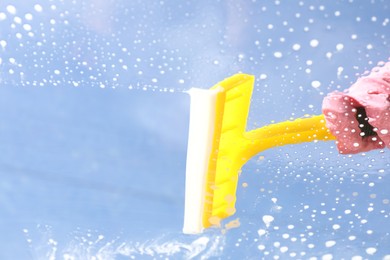 Woman washing window with squeegee tool against blue sky, closeup