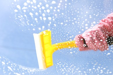 Woman washing window with squeegee tool against blue sky, closeup