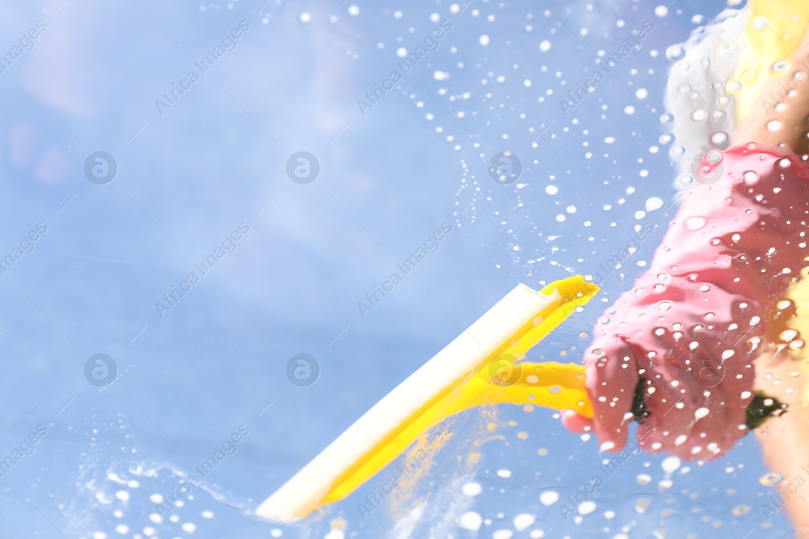 Photo of Woman washing window with squeegee tool against blue sky, closeup