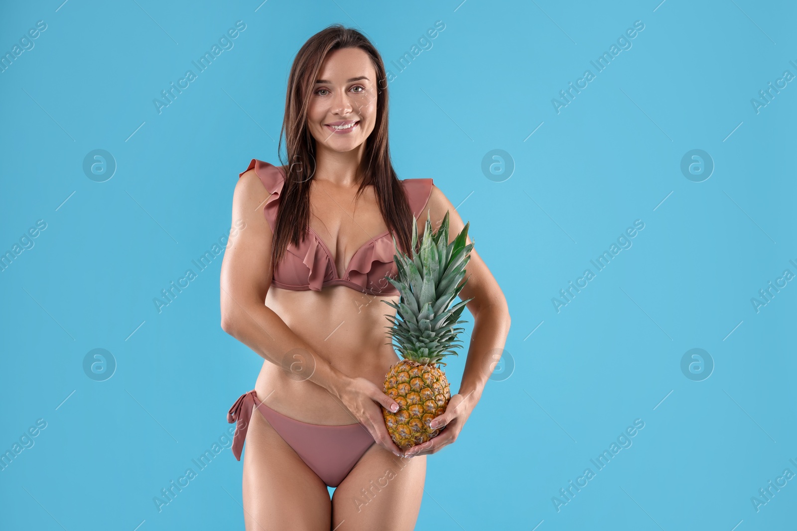 Photo of Woman in bikini with fresh pineapple on light blue background