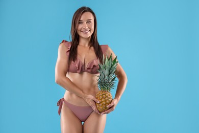 Woman in bikini with fresh pineapple on light blue background