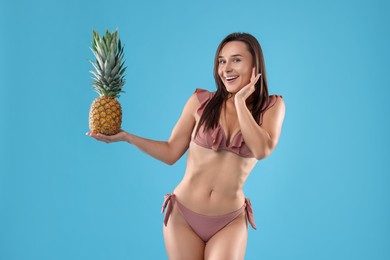 Photo of Woman in bikini with fresh pineapple on light blue background