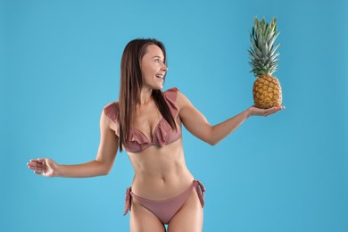 Photo of Woman in bikini with fresh pineapple on light blue background