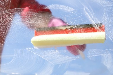 Woman washing window with squeegee tool against blue sky, closeup