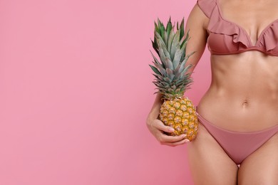 Woman in stylish bikini with fresh pineapple on pink background, closeup. Space for text