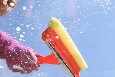 Woman washing window with squeegee tool against blue sky, closeup