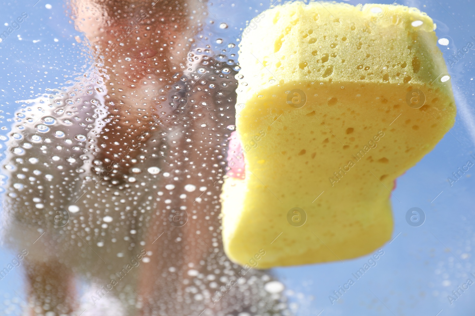 Photo of Woman washing window with sponge against blue sky, closeup