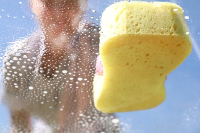 Photo of Woman washing window with sponge against blue sky, closeup