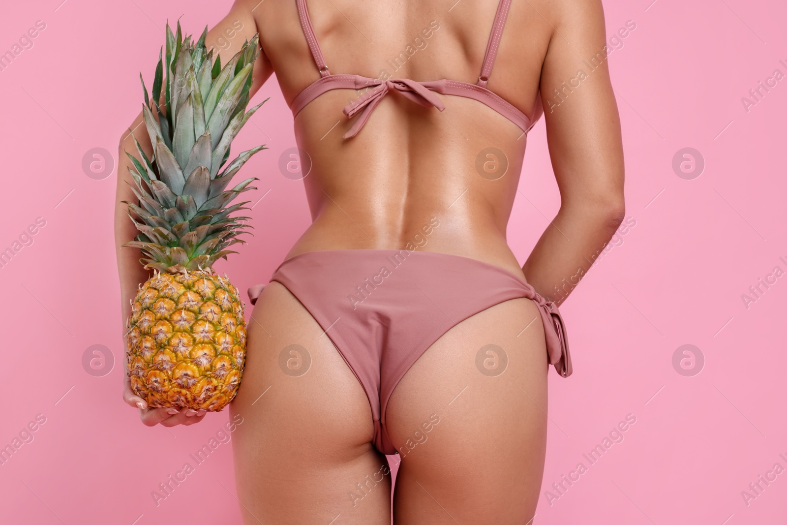 Photo of Woman in stylish bikini with fresh pineapple on pink background, closeup