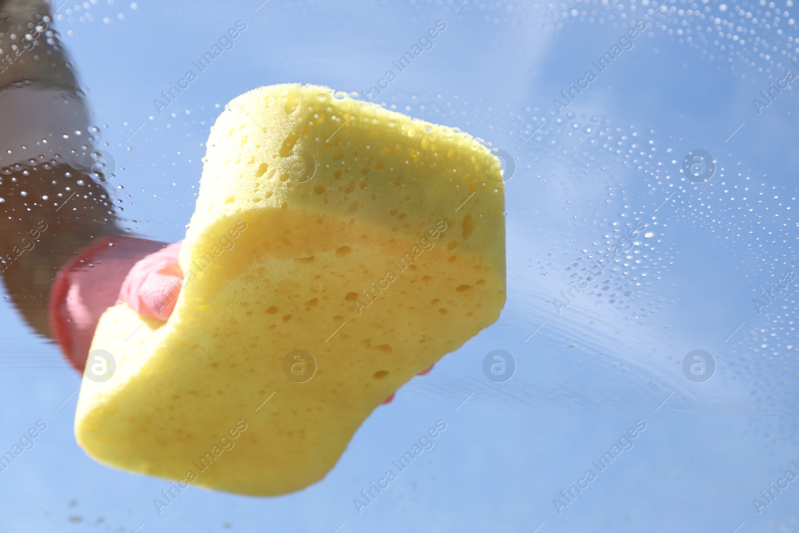 Photo of Woman washing window with sponge against blue sky, closeup