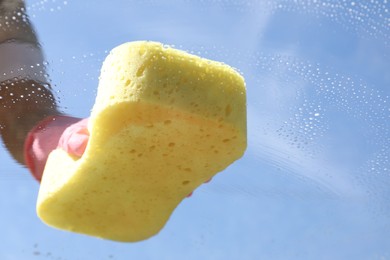 Photo of Woman washing window with sponge against blue sky, closeup