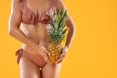 Photo of Woman in stylish bikini with fresh pineapple on orange background, closeup. Space for text