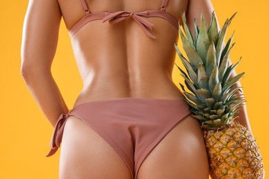 Photo of Woman in stylish bikini with fresh pineapple on orange background, closeup