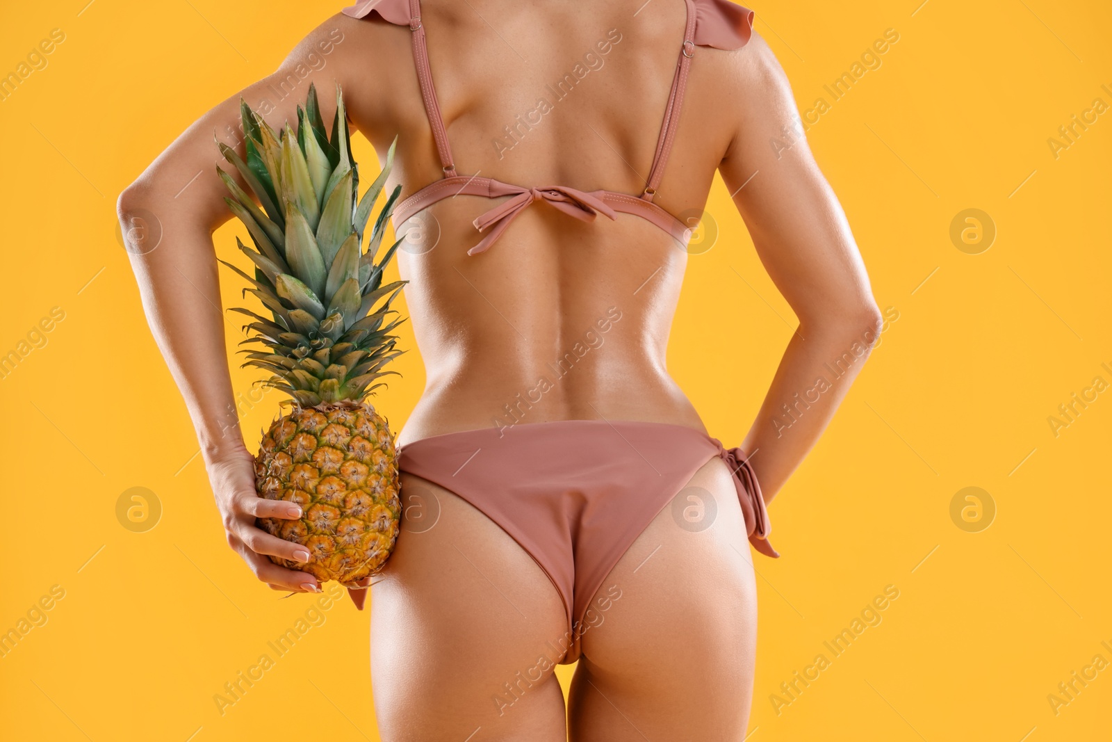 Photo of Woman in stylish bikini with fresh pineapple on orange background, closeup