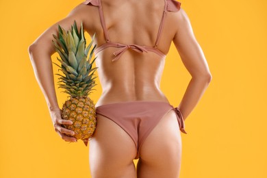 Woman in stylish bikini with fresh pineapple on orange background, closeup