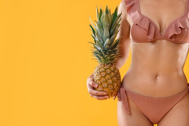 Woman in stylish bikini with fresh pineapple on orange background, closeup. Space for text